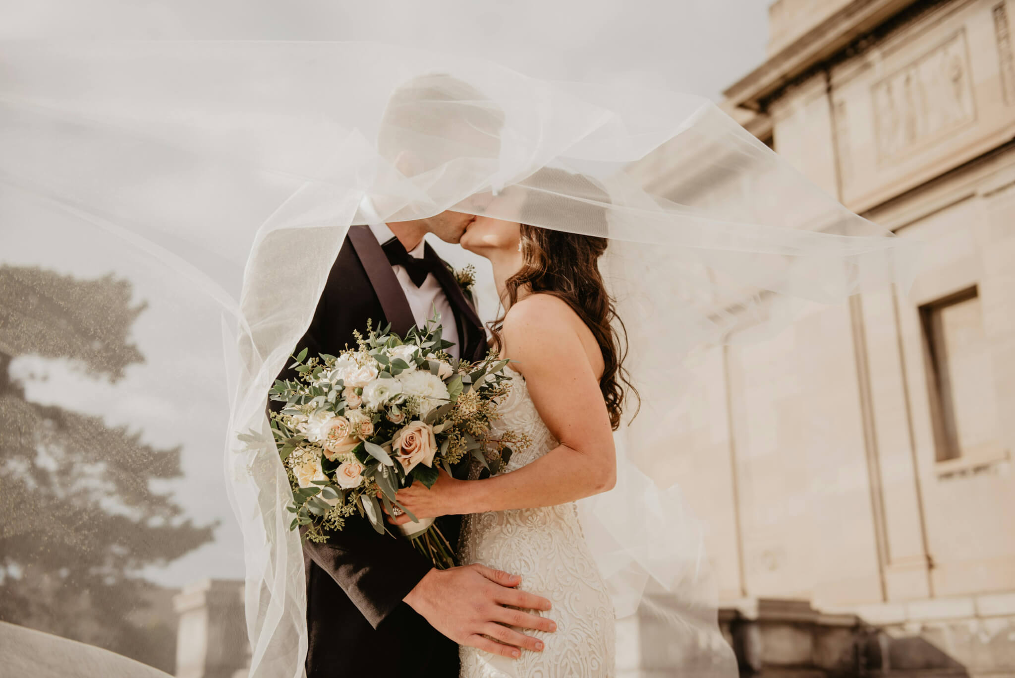 Beautiful image of newlyweds kissing, surrounded by the bride's veil and a large bouquet of beautiful flowers.