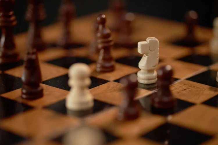 Close-up of a chessboard with wooden and black squares, showing chess pieces in mid-game.
