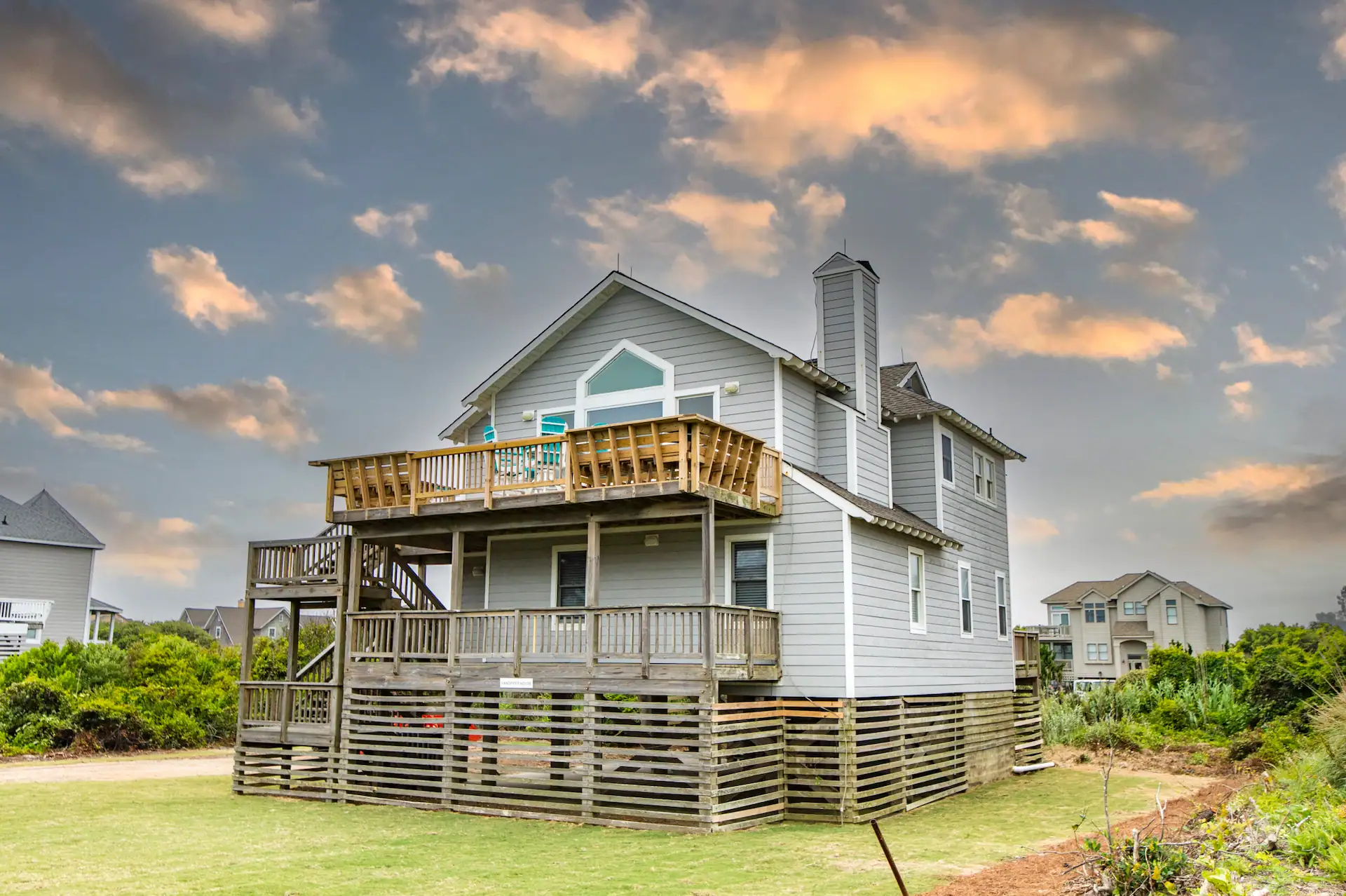 Facade of one of The Sanderling Resort residences, surrounded by lush greenery, under a blue sky with red clouds.