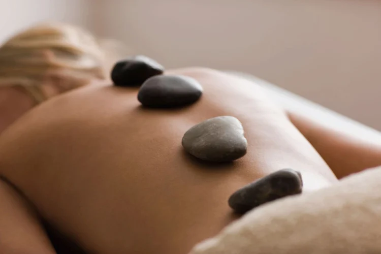 Woman fully relaxing while receiving a hot stone back treatment at the spa of The Sanderling Resort.