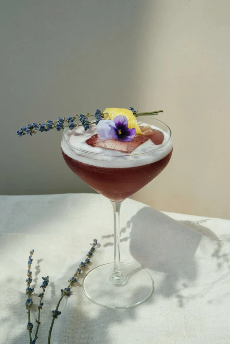 Spectacular martini cocktail in a rounded glass, decorated with flowers and lemon peel, placed on a linen cloth.